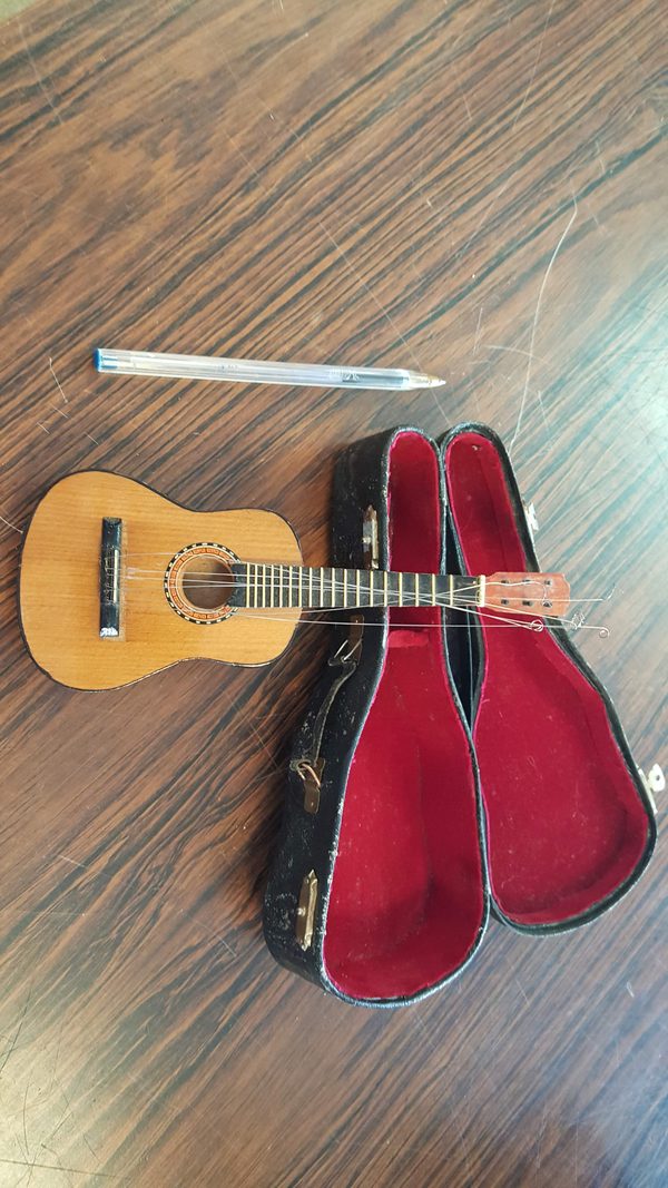 Miniature acoustic guitar with case, next to a pen for scale